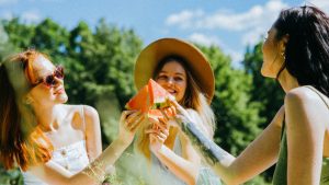 Three friends sharing watermelon on a sunny day, celebrating friendship outdoors.
