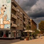 Street view of urban street art on building with dramatic clouds above.