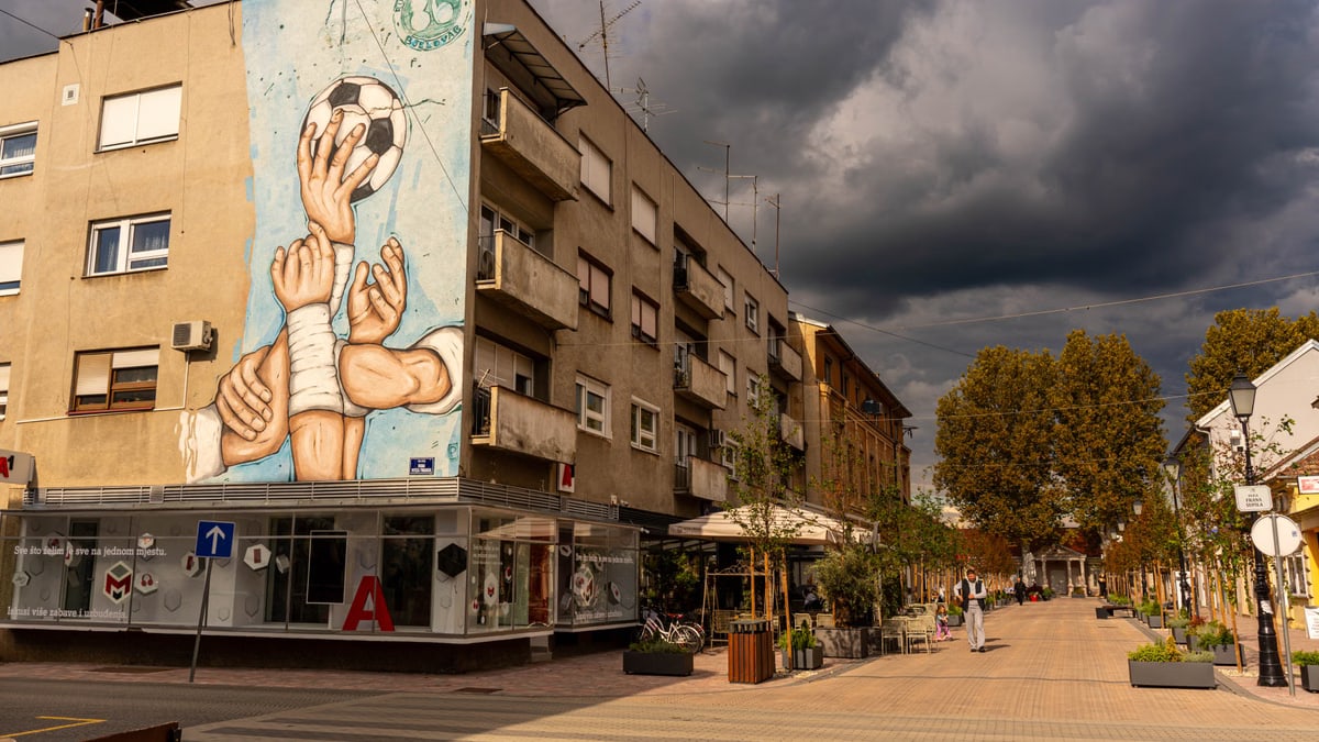 Street view of urban street art on building with dramatic clouds above.
